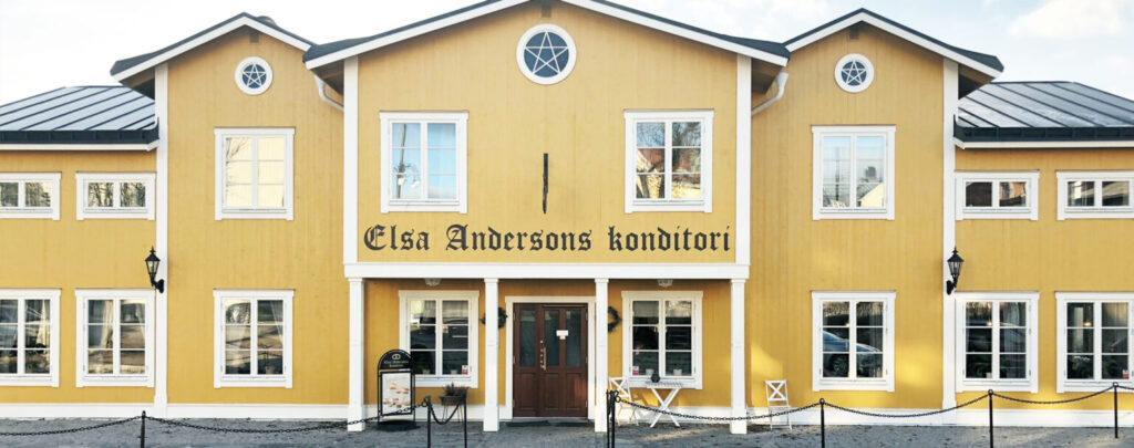 Framifrån vy av Elsa Andersons konditori, en gul byggnad med vita fönster och en välkomnande entré.